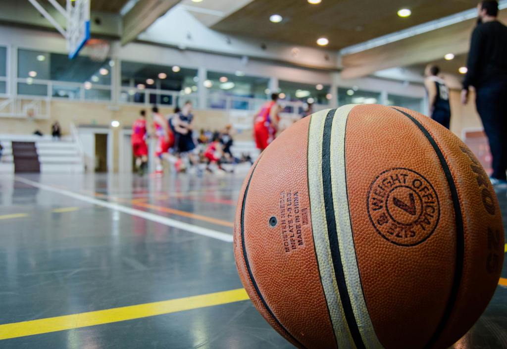 A basketball sits on the floor of an indoor practice gym with people playing the background