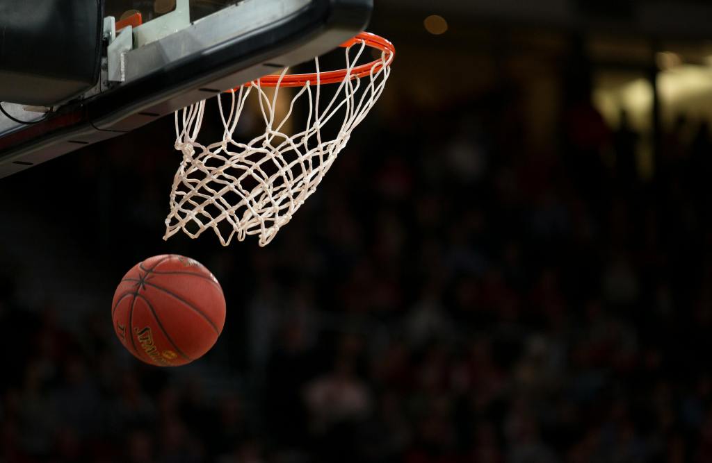 A basketball goes through a hoop in a darkened arena