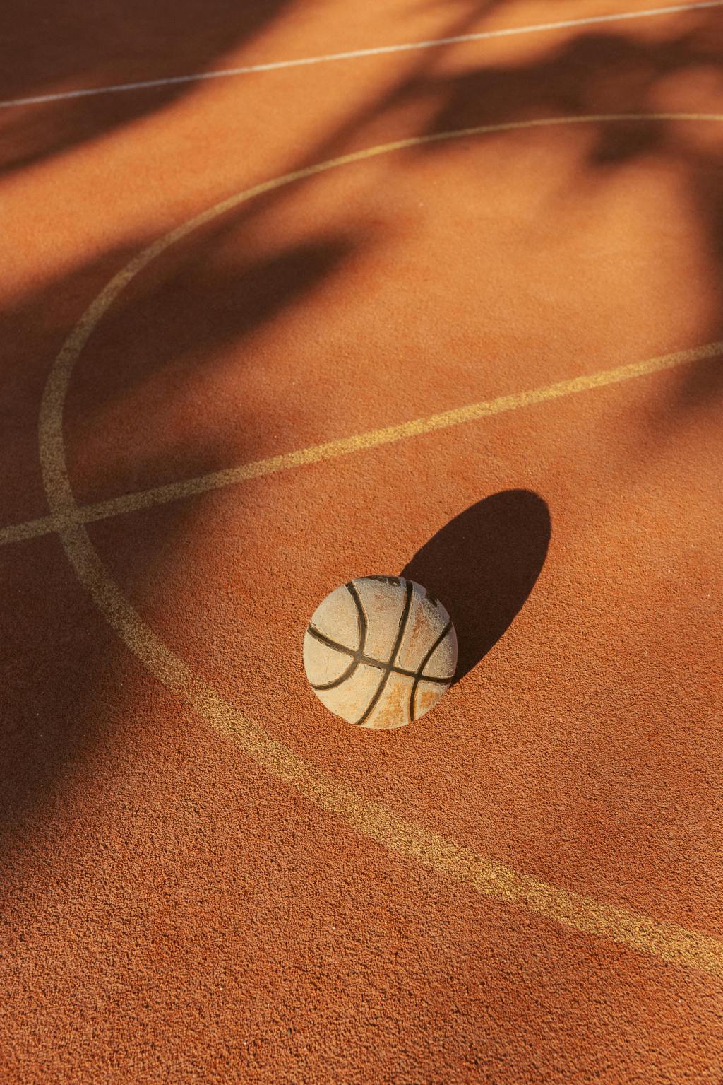 A basketball sits on an empty outdoor court near the center circle.