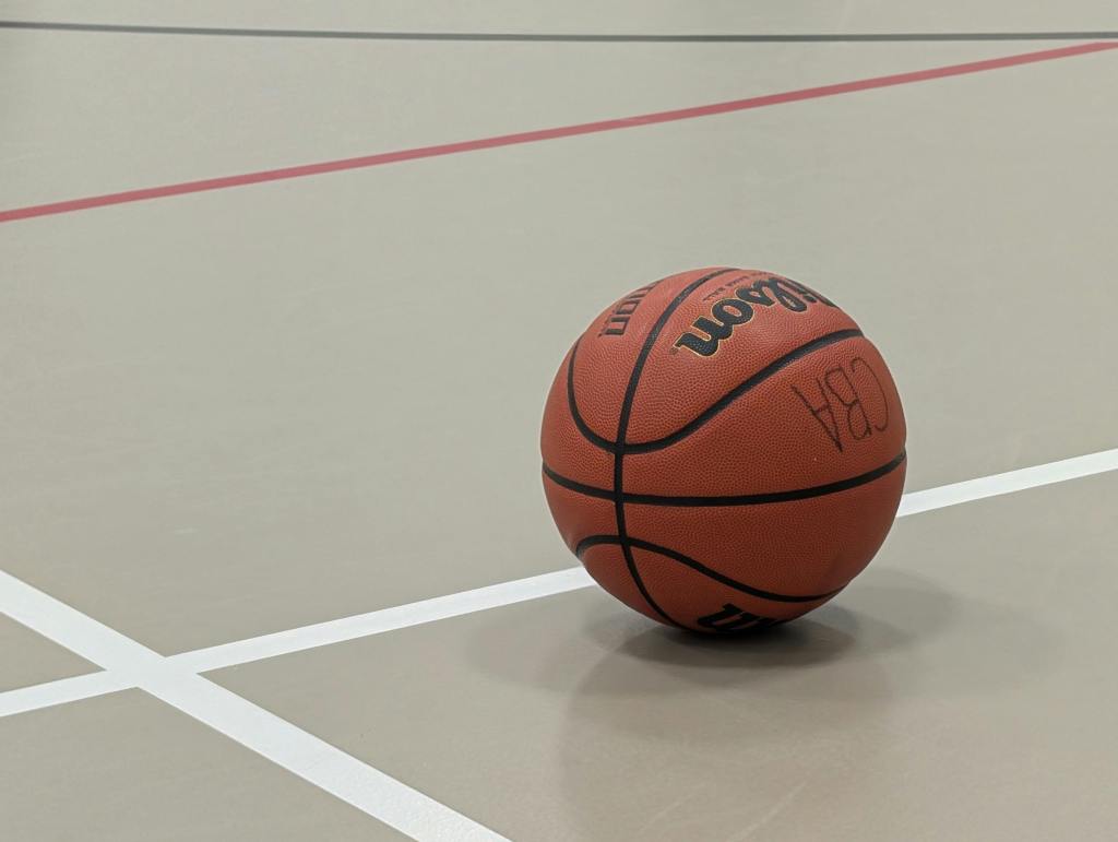 A basketball sits on the floor in an indoor basketball court.